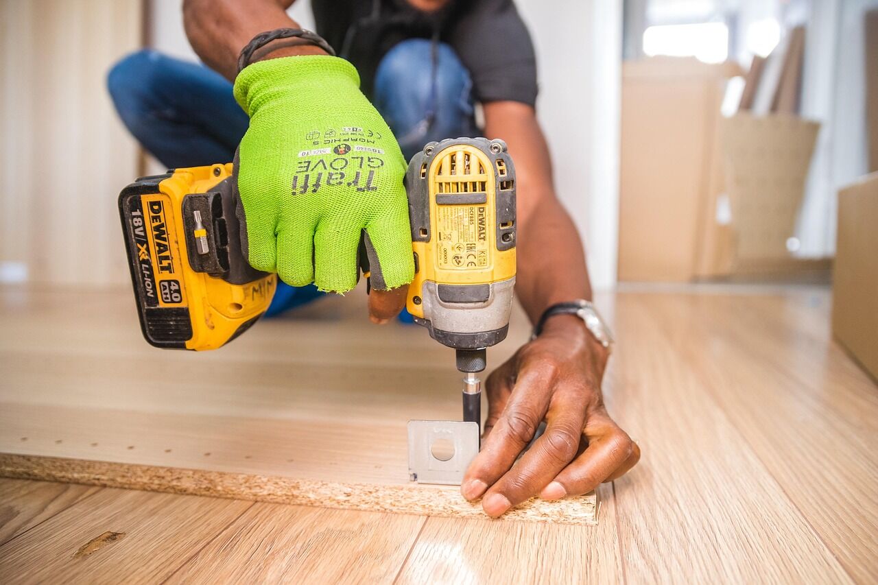 Gloved hands using a cordless drill on a wood floor