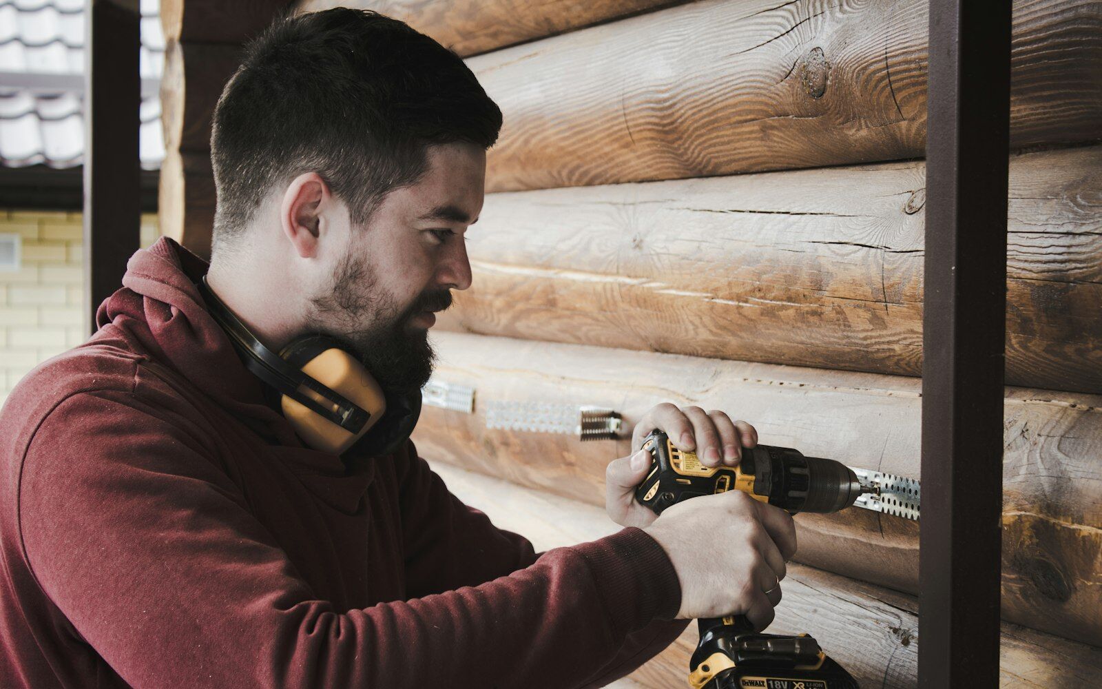 Man wearing ear protection using a drill on a wood wall