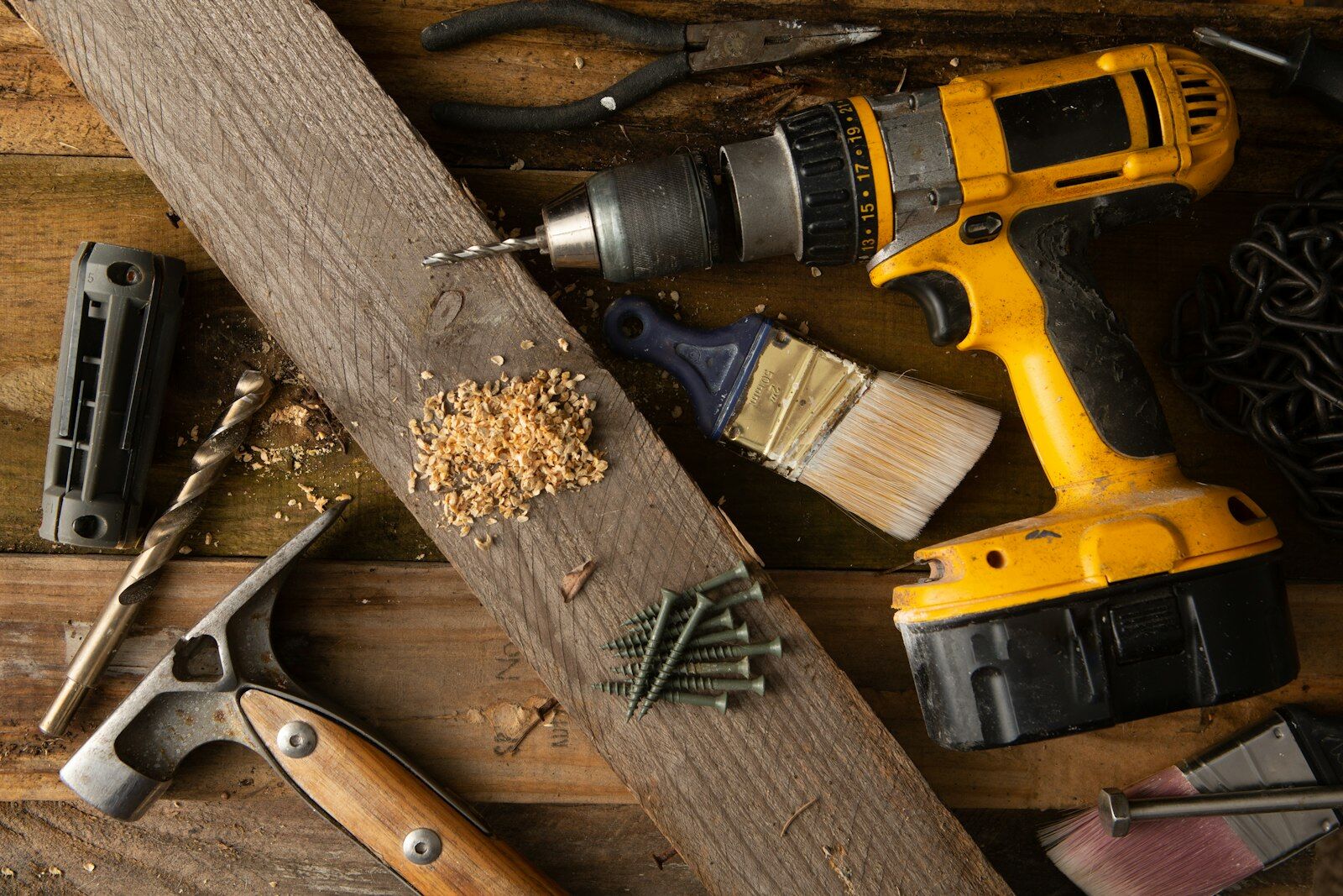 Yellow drill, paintbrush, nails and hand tools on a wooden table
